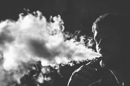 A man is vaping and blowing big plumes of smoke around him, he is struggling with vape addiction