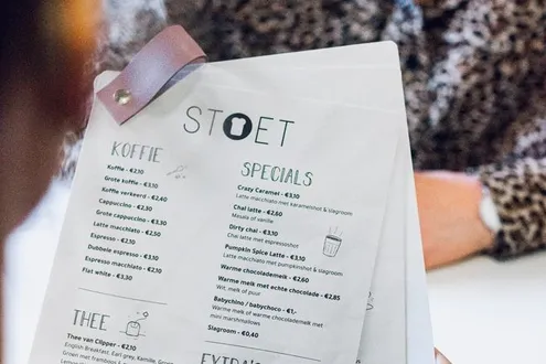 A woman is sat at a restaurant table opposite another person she is looking at a menu which includes calorie information
