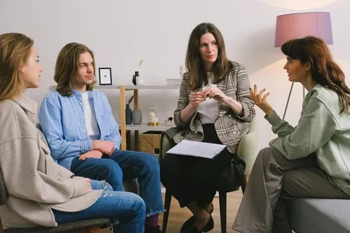 Four people sitting in a comfortable and calming space, one of them is leading the group session
