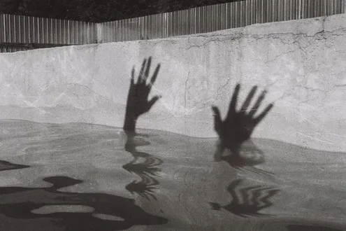 A shadow of two hands reaching up on a wall surrounded by water representing the link between addiction and suicide