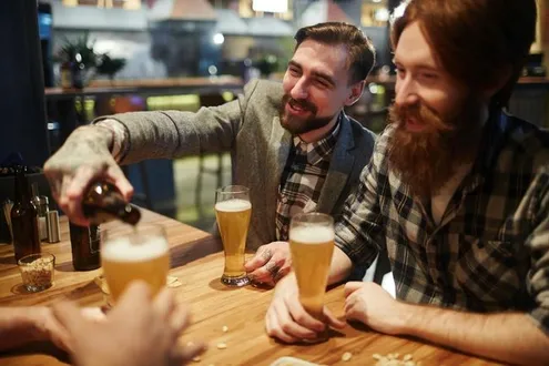 Men sit around a table at a pub pouring alcoholic drinks for one another sober shaming each other into drinking alcohol