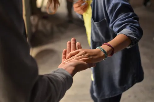 A person with an outstretched hand reaches to another persons hand to support them as they are struggling with addiction
