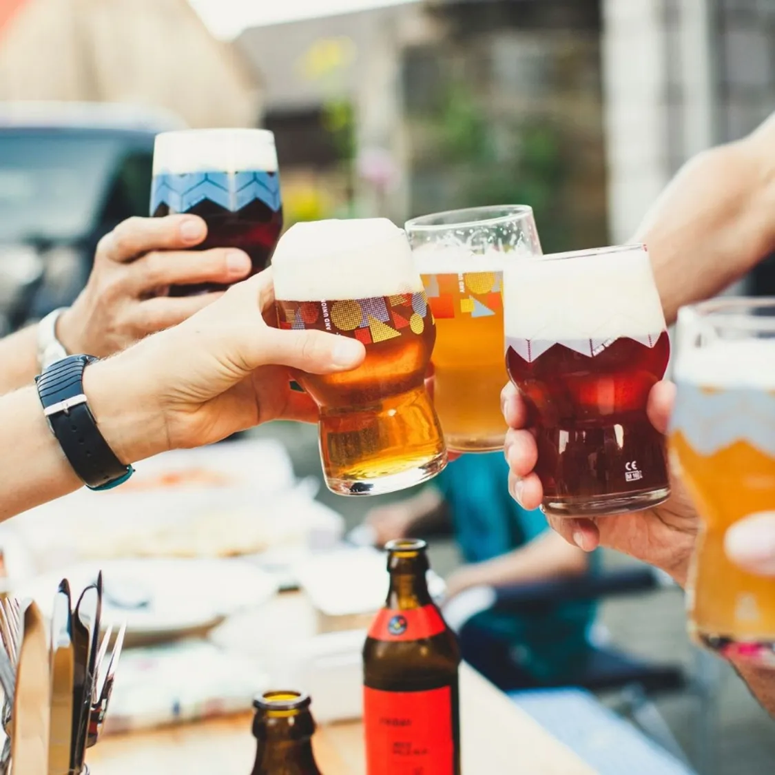 five pints of beer with people clinking glasses