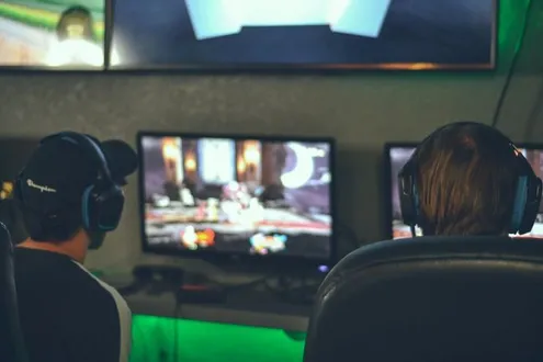 Two boys with headsets sit in front of a gaming set up playing computer games highlighting gaming addiction