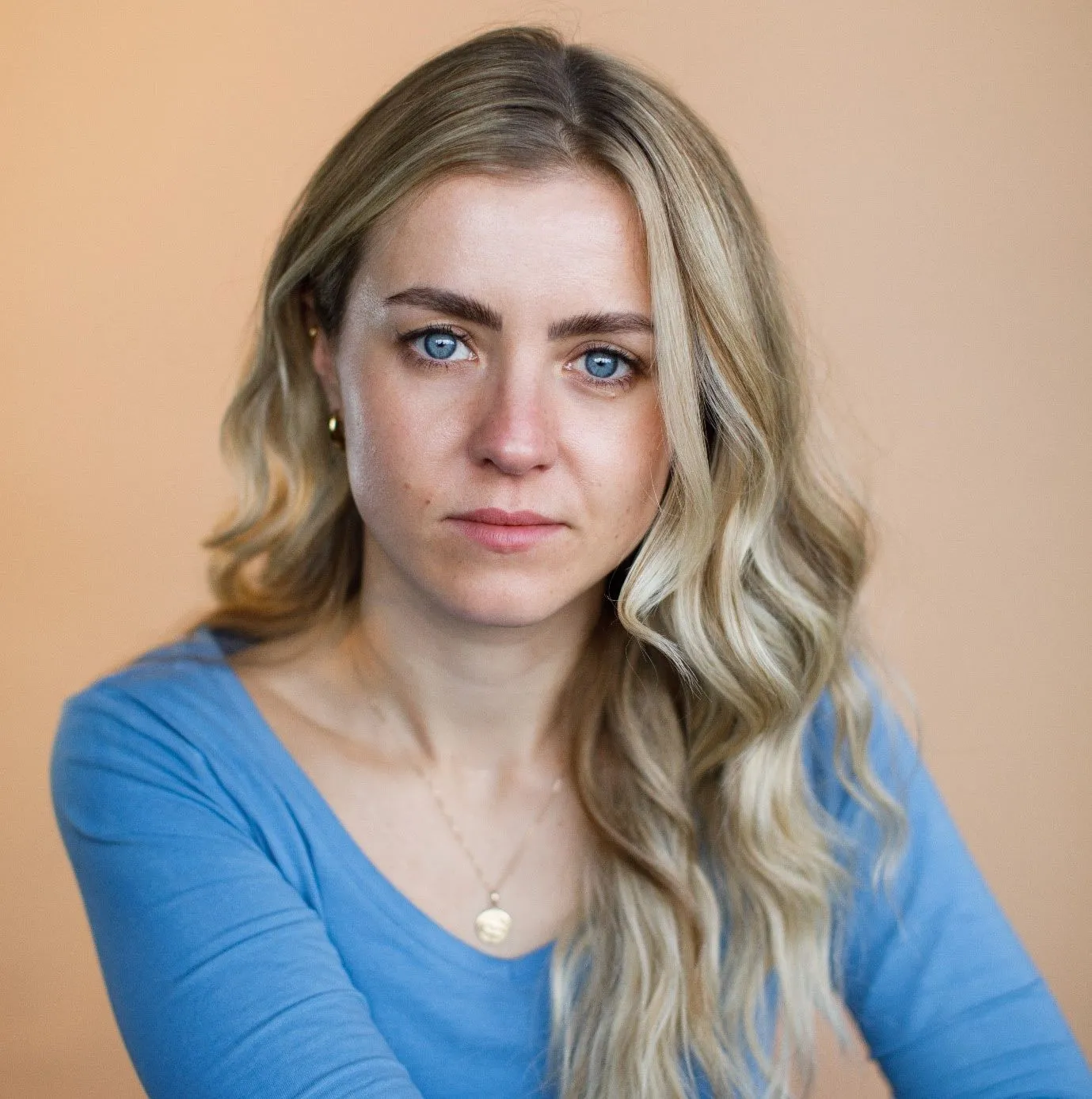 Isabelle Hawkins with long blonde hair and blue eyes wearing a light blue top, sitting indoors against a neutral background, representing professionalism and approachability.
