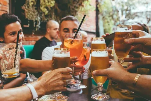 Group of men and women sat around a table they are raising their glasses of alcohol to one another to say cheers