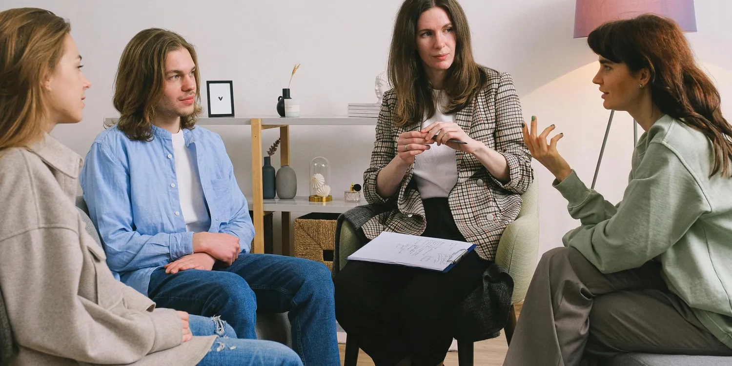 Four people sitting in a comfortable and calming space, one of them is leading the group session