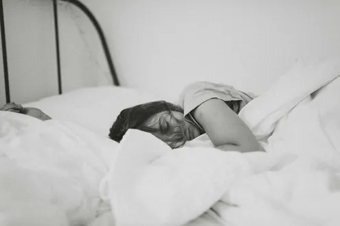 A woman is laying in bed trying to sleep highlighting what problems alcohol can cause on sleep