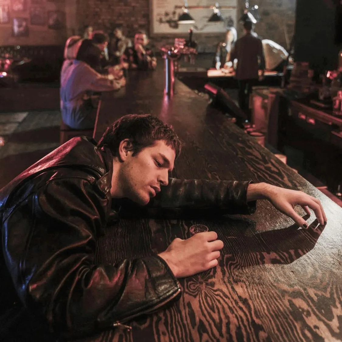 a male asleep at a bar with a shot glass in hand