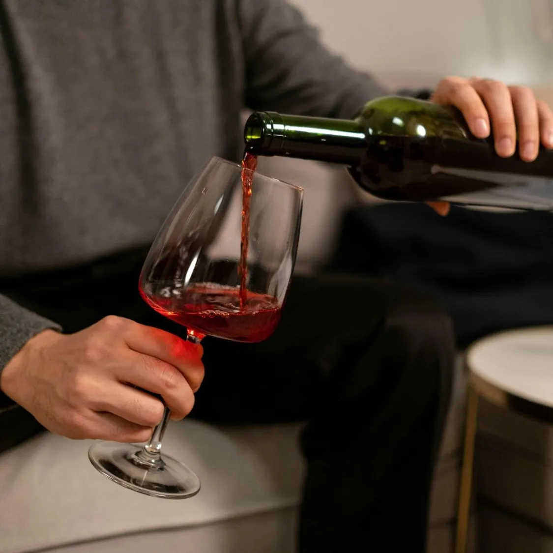 someone pouring red wine from a green bottle into a large wine glass
