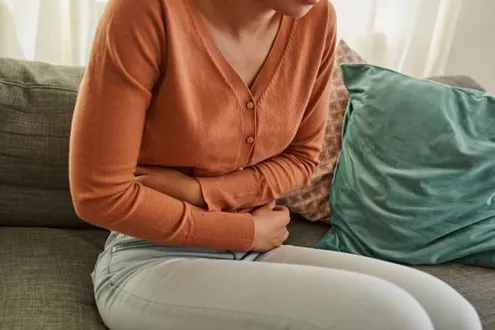 A woman sits on a sofa cradling her stomach showing how alcohol can impact on stomach pains and problems