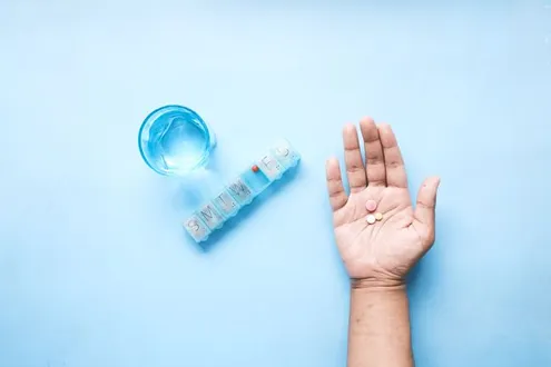 A hand outstretched holds tramadol pills next to a pill box and glass of water highlighting how it impacts the brain