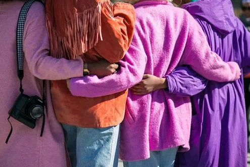 A group of women with arms wrapped around one another are supporting each other in long term recovery from substance addiction