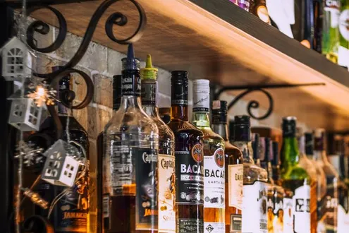 A row of bottles containing various spirits sit on a lit bar highlighting the effects of alcohol poisoning & how long it lasts