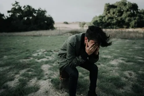 A man is sitting on a bollard in the countryside, he has his head in his hands depressed, he cannot stop thinking about cocaine